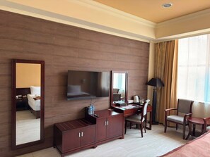 A hotel room with a bed, a desk with a chair, a television, a mirror, and a window with curtains. - Royal Grand Hotel (Monrovia)