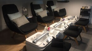 A spa room with black chairs, a massage table, and a sink with various toiletries. - Royal Grand Hotel (Monrovia)