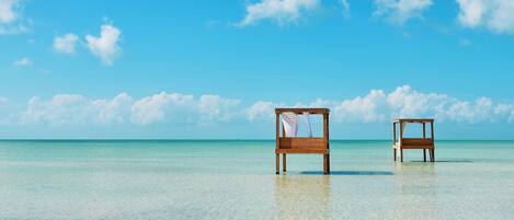 Two wooden beach chairs on a clear turquoise sea with a bright blue sky.