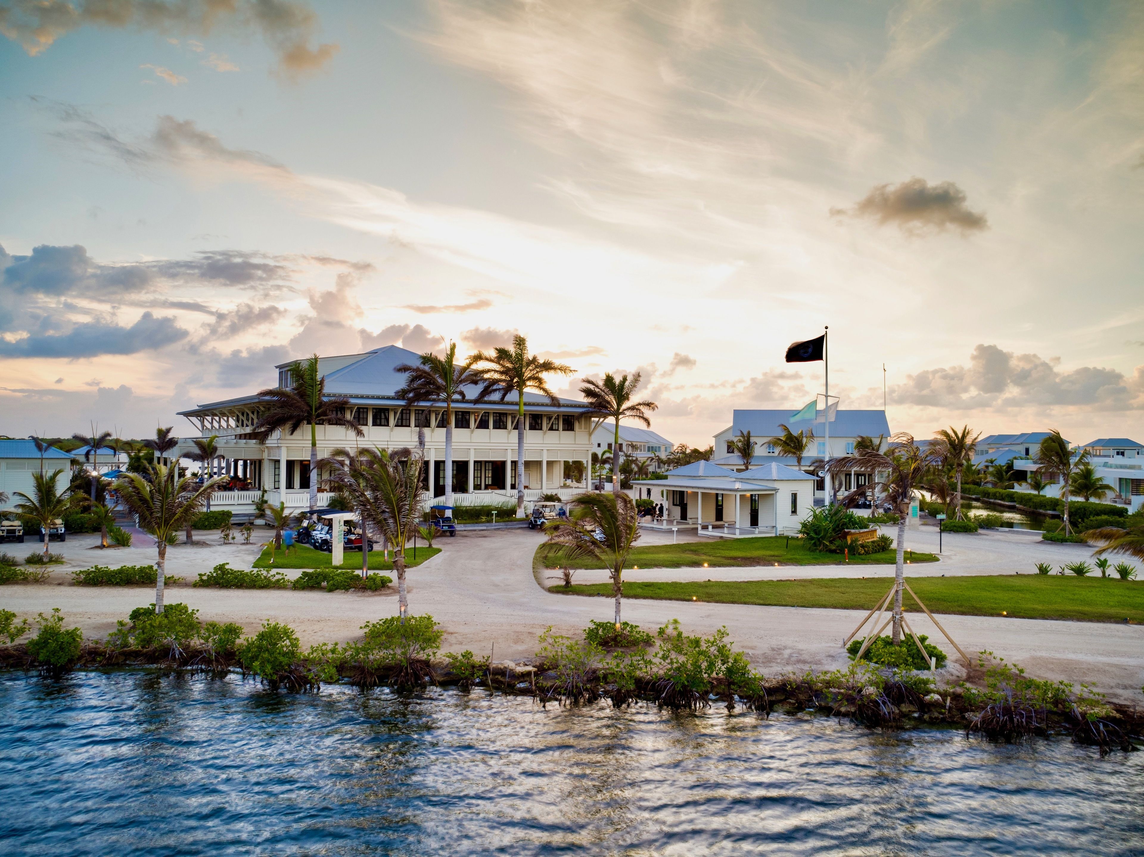 A beachfront hotel with a large building, palm trees, and a flag.