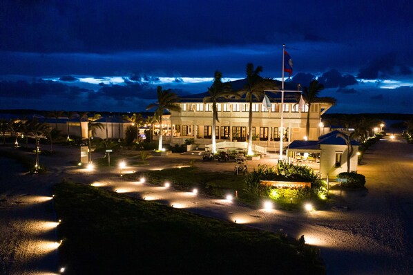 A large, multi-story hotel with a prominent flag, well-lit pathways, and palm trees. - Mahogany Bay Resort & Beach Club, Curio Collection by Hilton (San Pedro)