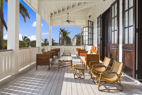 A covered outdoor seating area with wooden furniture, a ceiling fan, and large windows.