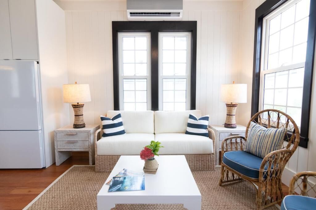 A cozy living room with a white sofa, two side tables with lamps, a wicker chair, and a coffee table with a magazine.