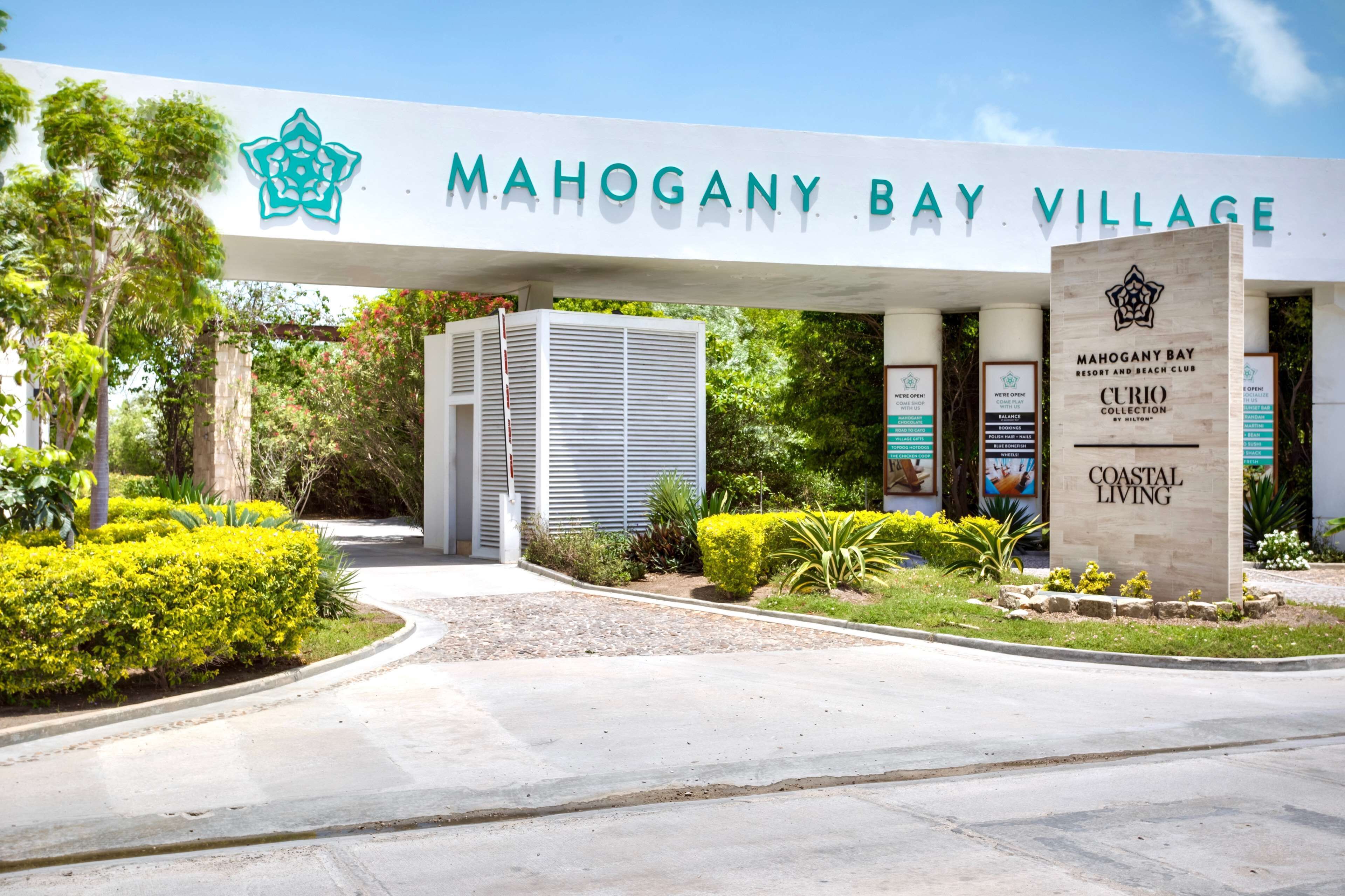 L’entrée de Mahogany Bay Village est signalée par un panneau indiquant le nom et les logos du complexe hôtelier et du club de plage.