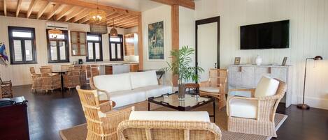 A spacious living area with wicker furniture, a white sofa, a glass coffee table, and a television mounted on the wall.