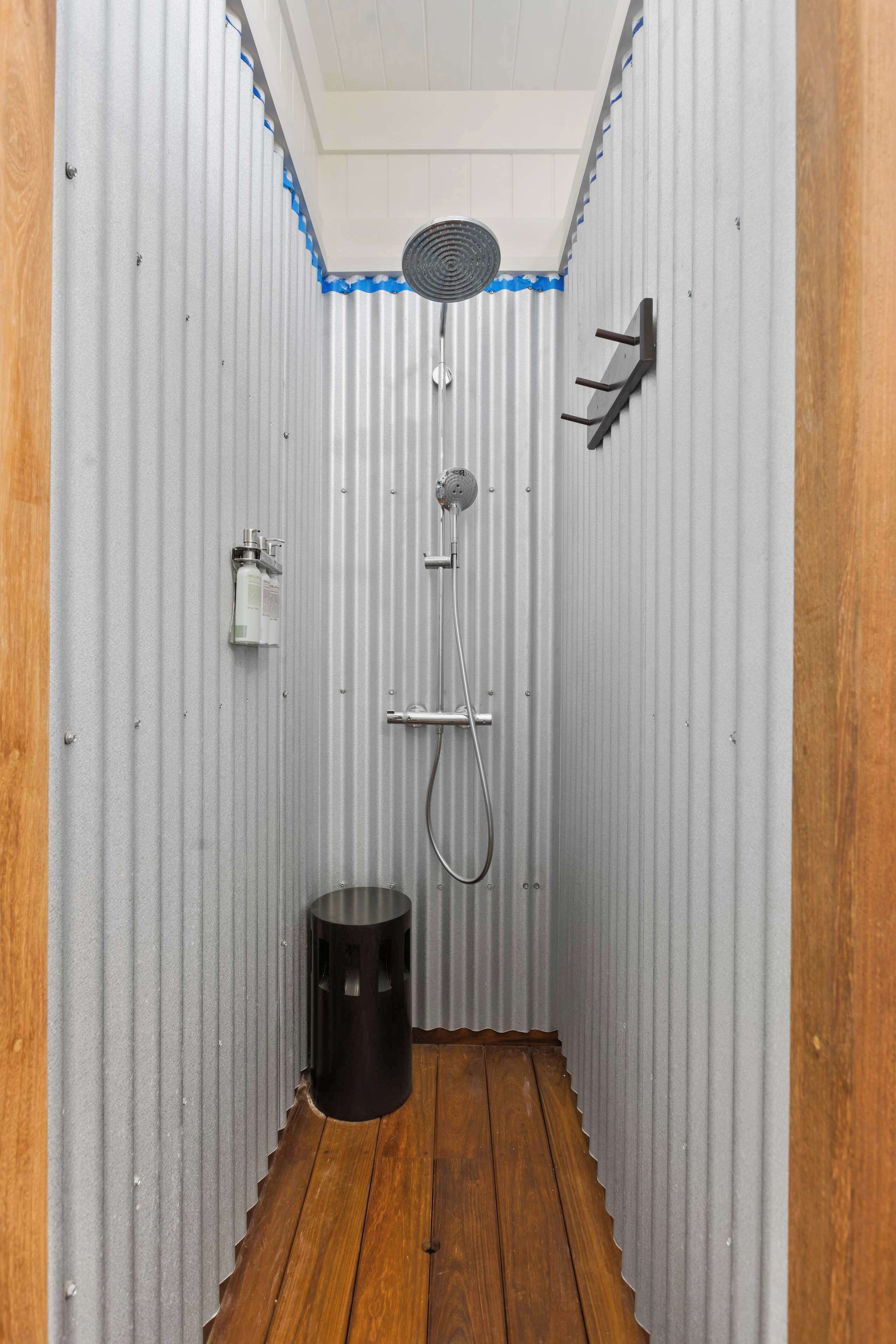 Un espacio de ducha pequeño y cerrado, con suelo de madera, un cabezal de ducha de mano, un grifo empotrado en la pared y un ventilador.