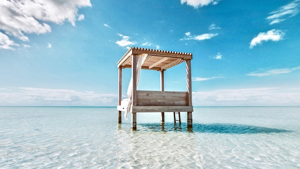 Eine Strandhütte aus Holz mit einem Sonnensegel, gelegen an einem klaren, blauen Meer mit flachem Wasser.