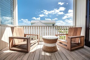 A wooden deck with two chairs and a round table, overlooking a house and a clear blue sky. - Mahogany Bay Resort & Beach Club, Curio Collection by Hilton (San Pedro)