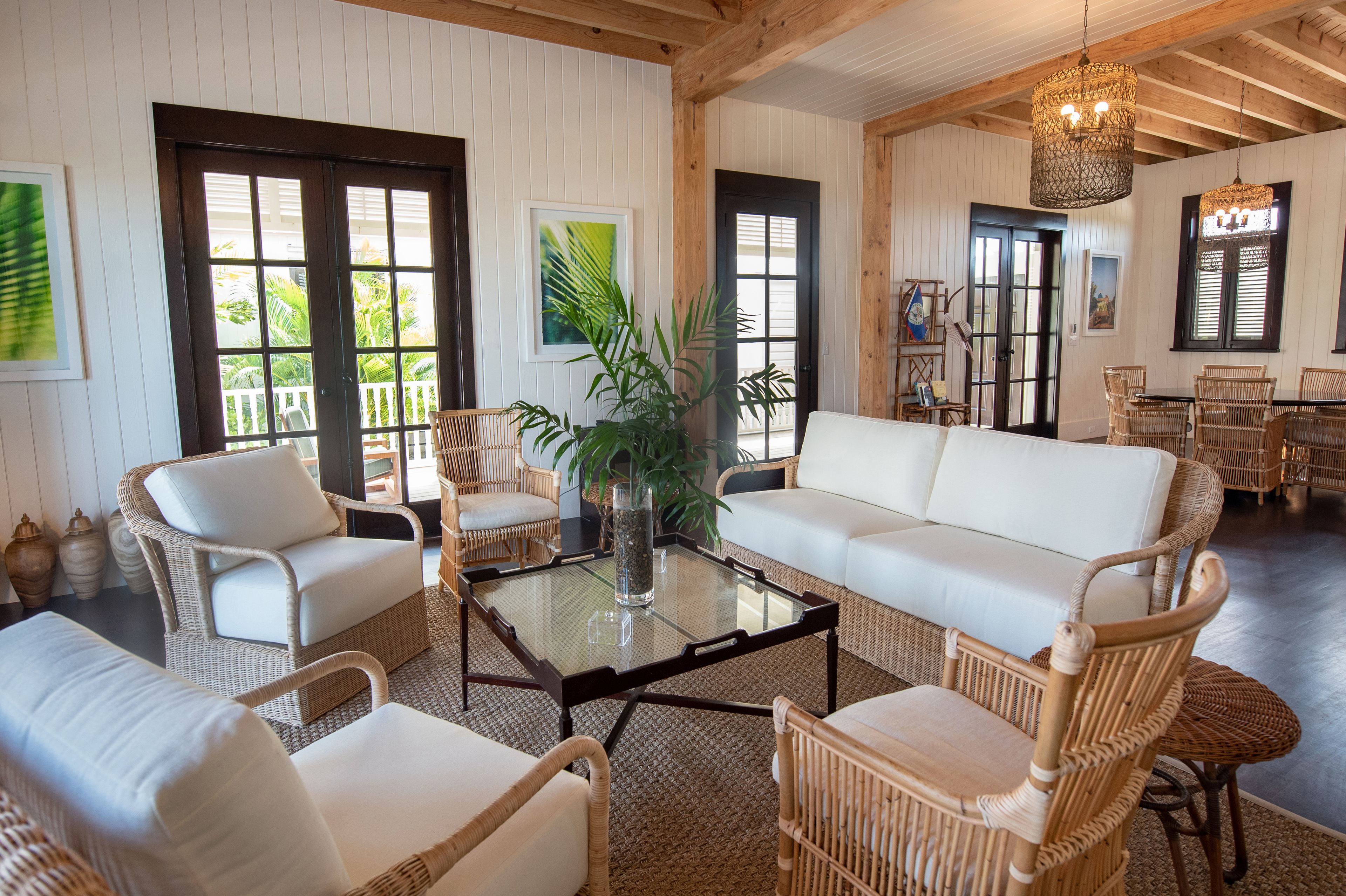 A spacious living area with a white sofa, wicker chairs, a glass coffee table, and a large potted plant.
