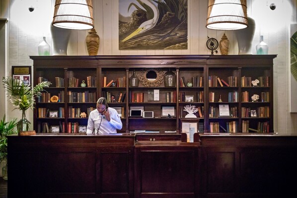 Una recepción con una recepcionista, rodeada por una amplia estantería llena de libros y objetos decorativos.