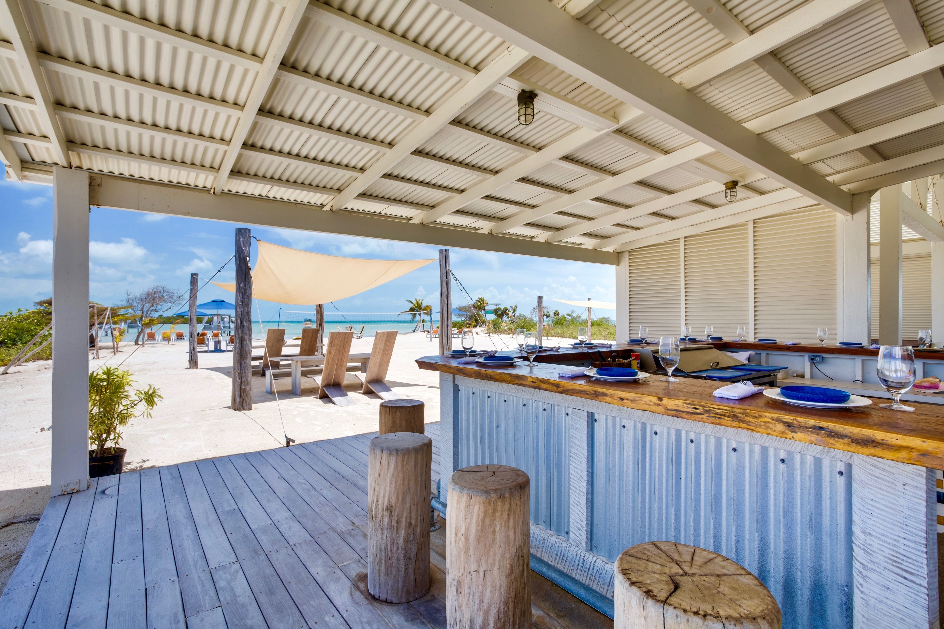 A beachside bar with a wooden deck, a view of the ocean, and beach chairs.