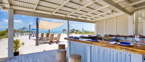 A beachside bar with a wooden deck, a view of the ocean, and beach chairs.