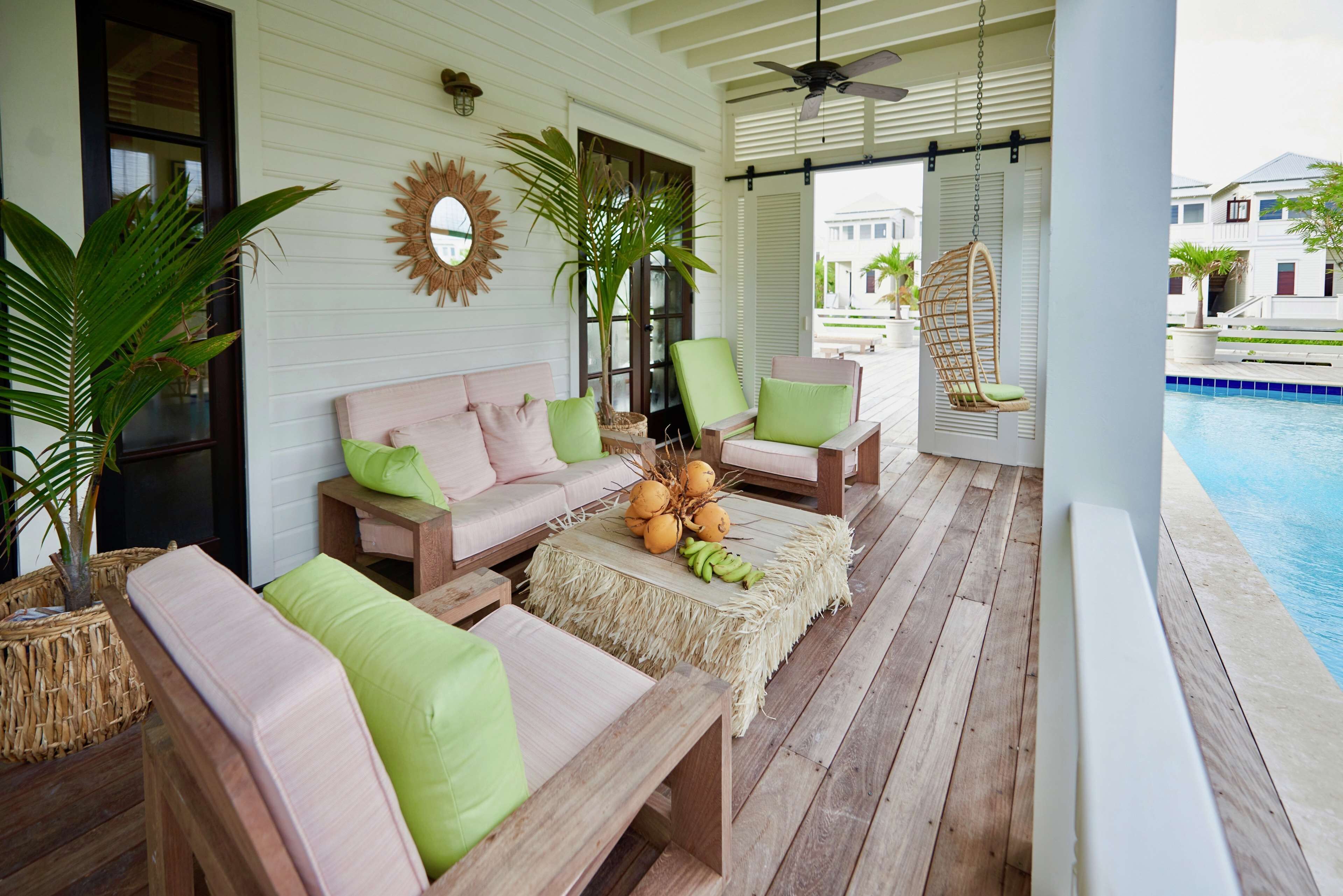 A covered outdoor seating area with a pool, wooden furniture, and tropical plants.