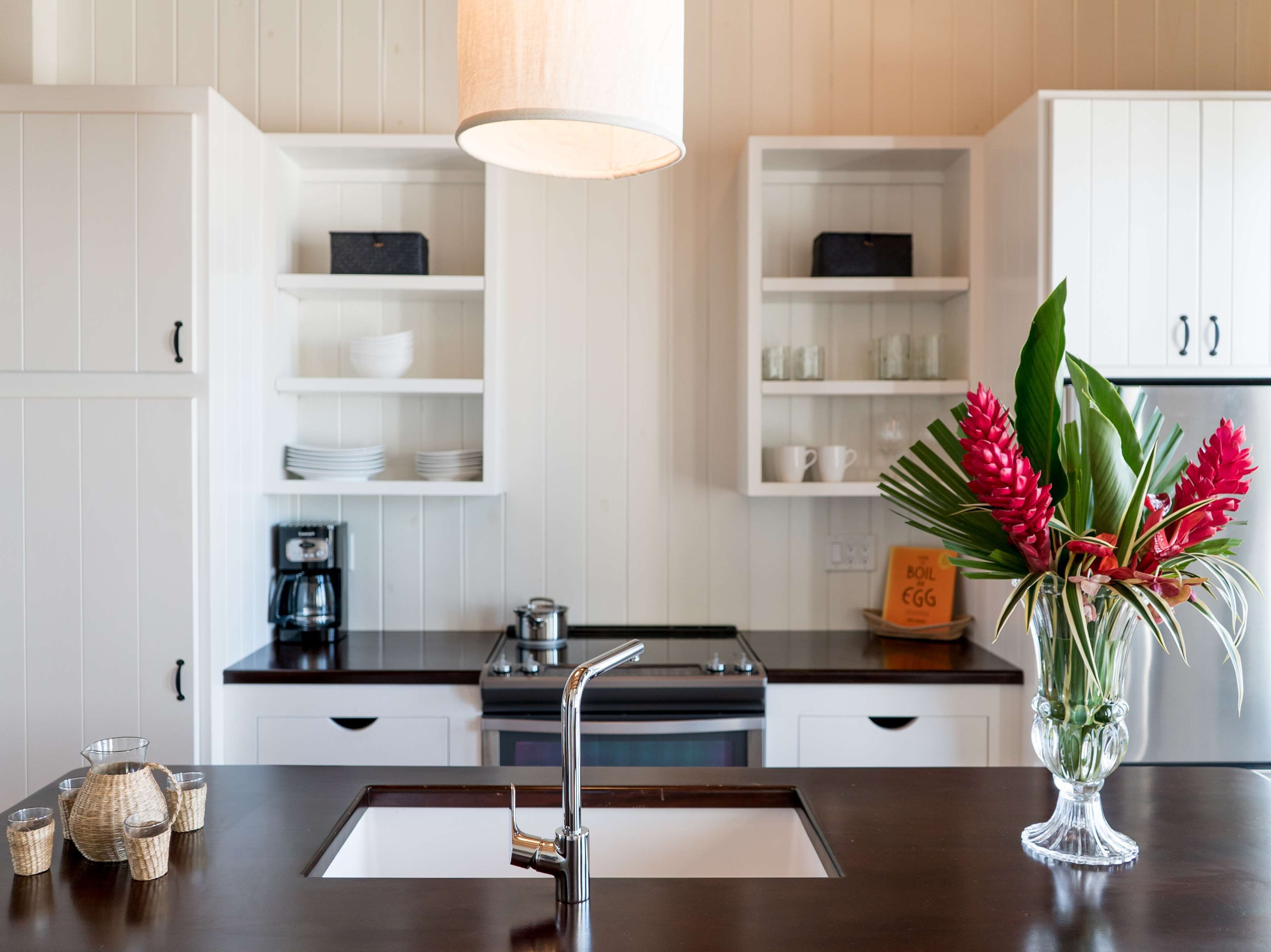 A modern kitchen with white cabinetry, a dark countertop, a stainless steel sink, and a vase with red flowers.