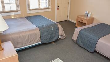 A hotel room with two beds, a nightstand, a lamp, and a door.