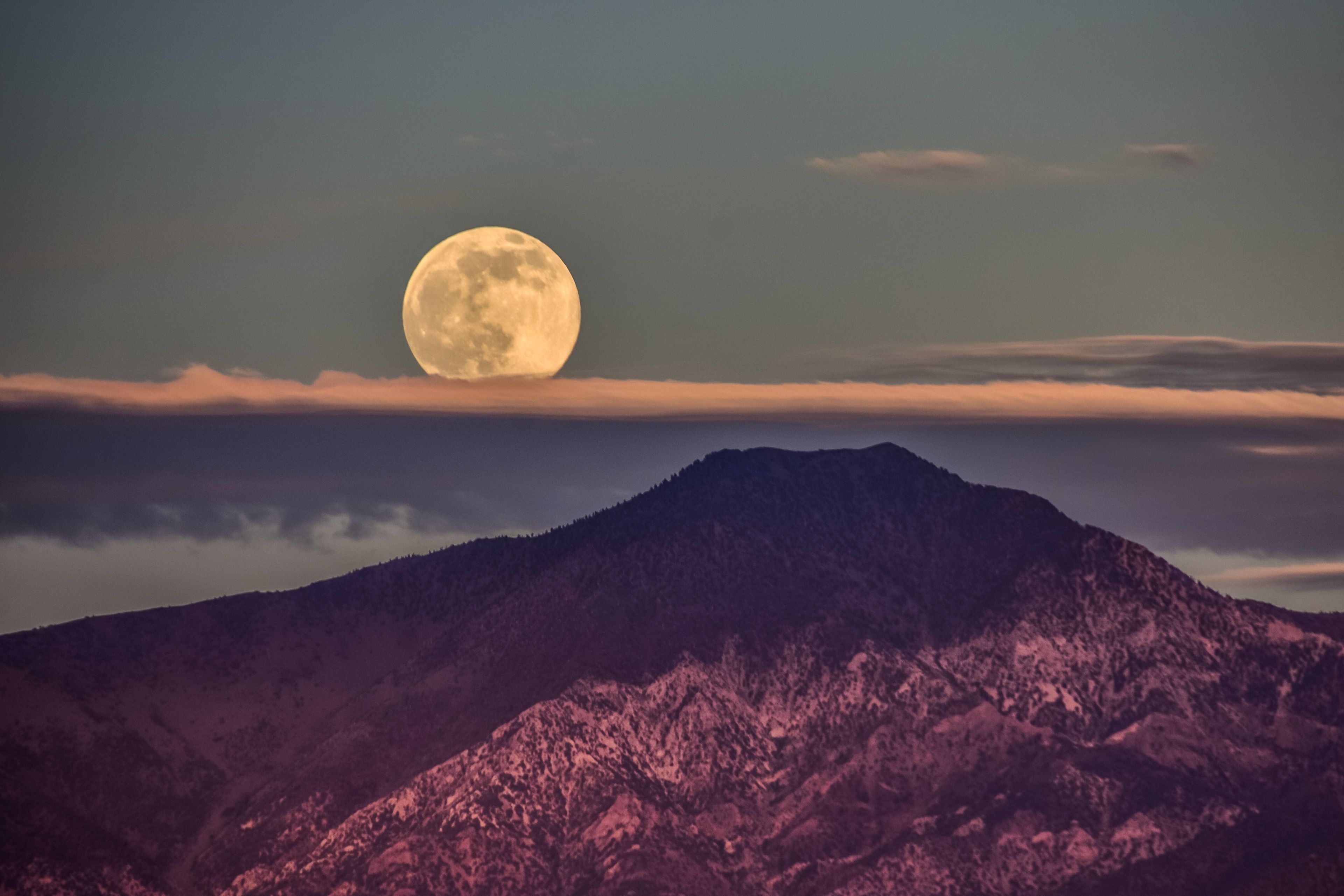 A mountain with a full moon in the sky.