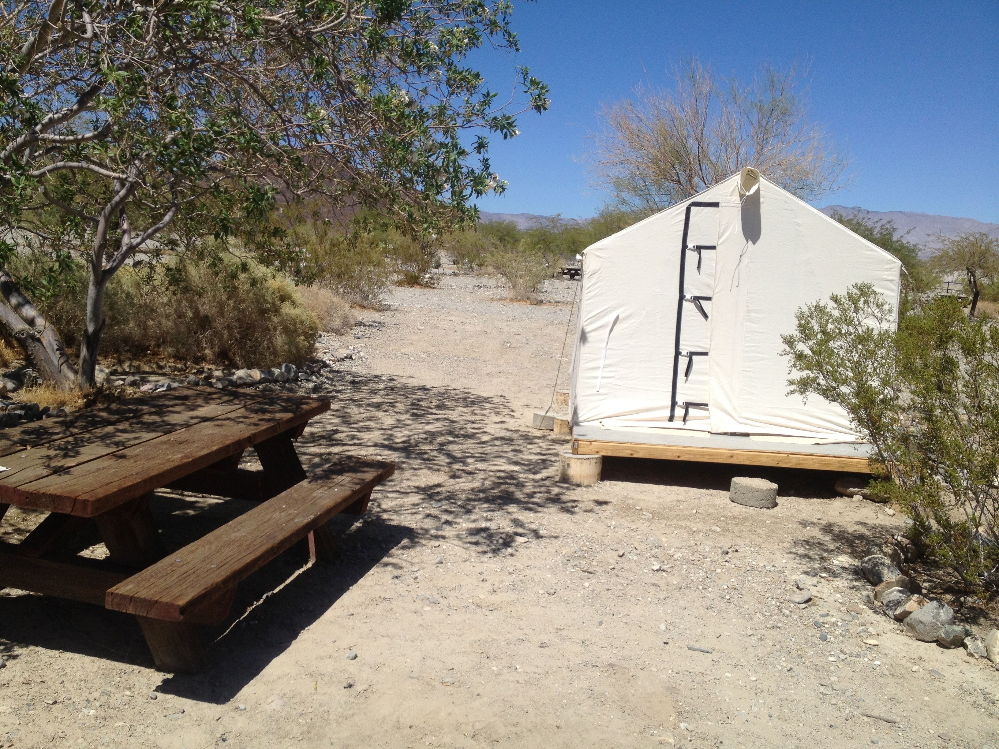 A tent set up on a gravel path with a picnic table nearby.
