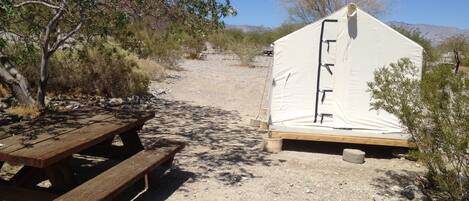 A tent set up on a gravel path with a picnic table nearby.