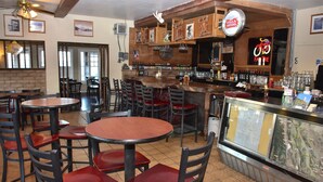 A restaurant interior with multiple tables and chairs, a bar area with a neon bicycle sign, and a menu display case. - Panamint Springs Resort (Panamint Springs)