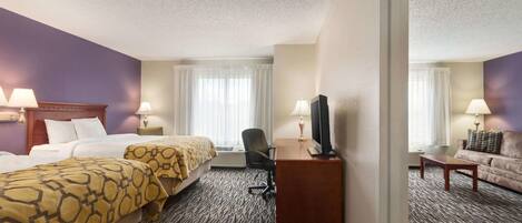 A hotel room with two beds, a desk, a chair, a television, and a sofa.