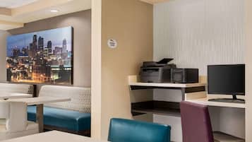 A hotel room with a cityscape painting, a business center with a printer and computer, and seating areas with blue and white upholstery.