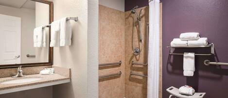 A bathroom with a sink, mirror, shower with grab bars, and a towel rack.