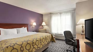 A hotel room with a large bed, two bedside lamps, a desk with a television, and a window with curtains.