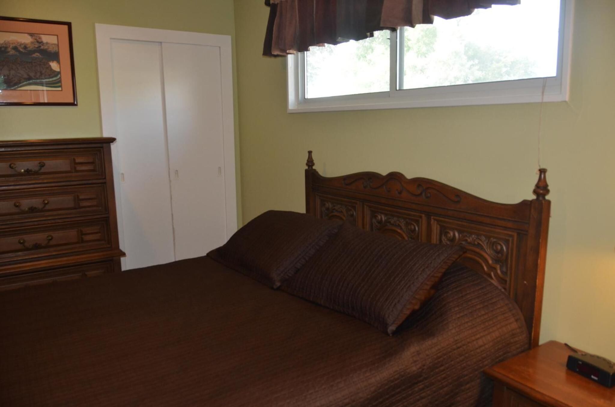 A bedroom with a wooden bed, a dresser, a window with curtains, and a door.