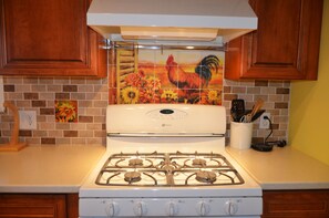 Una cocina con estufa a gas, armarios de madera y un salpicadero con diseño de gallo.