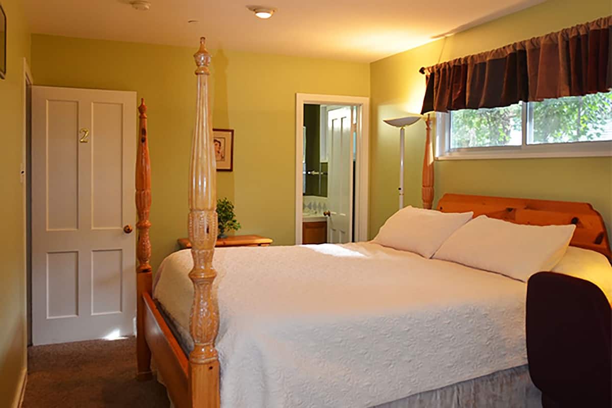 A four-poster bed with a white bedspread, a wooden headboard, and a nightstand with a lamp.