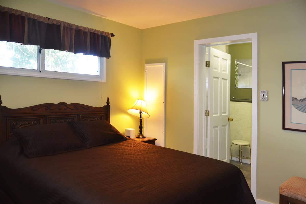 A bedroom with a large bed, a bedside lamp, a window with curtains, and a door leading to a bathroom.