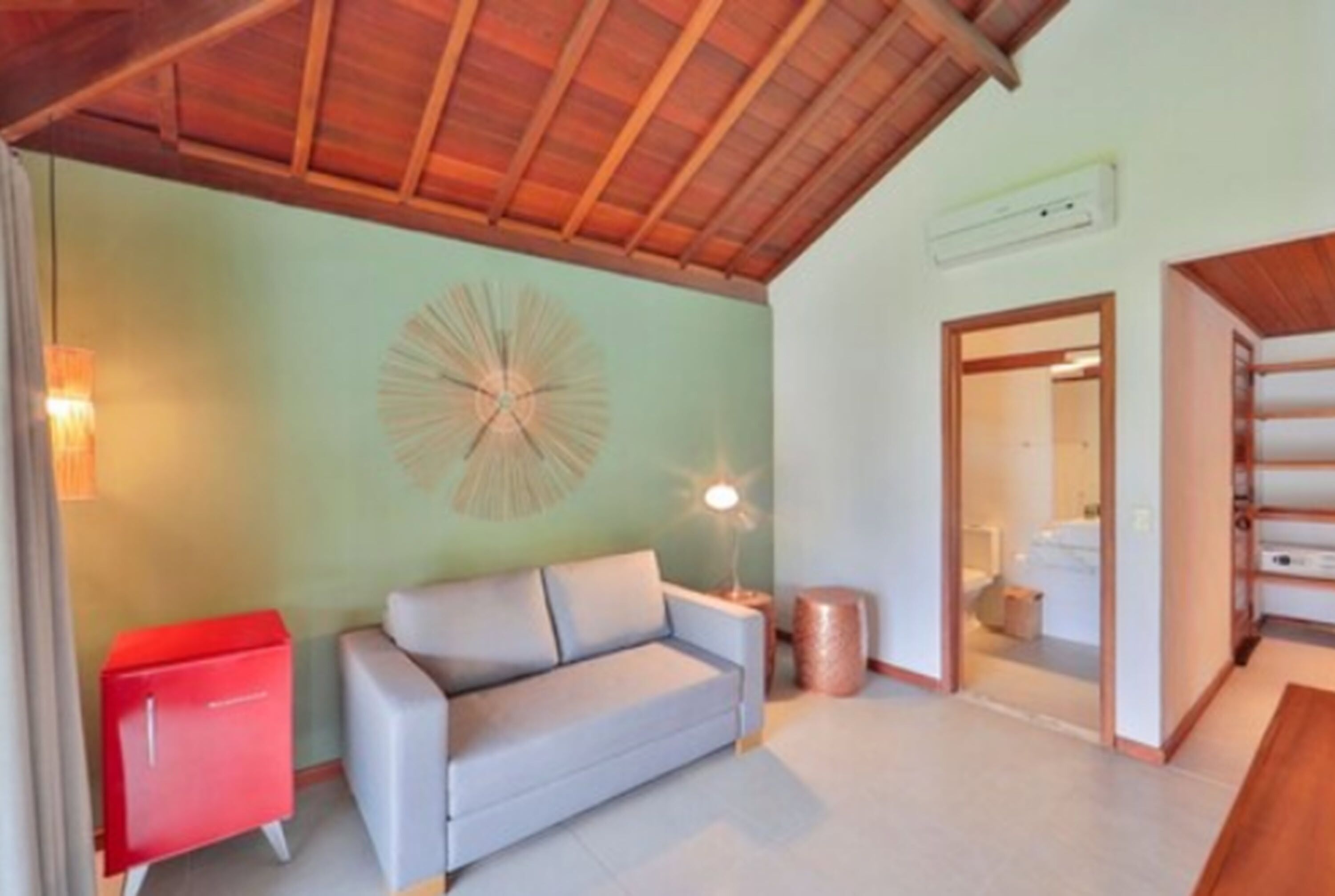 Una habitación con techo de madera, un sofá de color claro, un armario rojo y un aplique de pared.