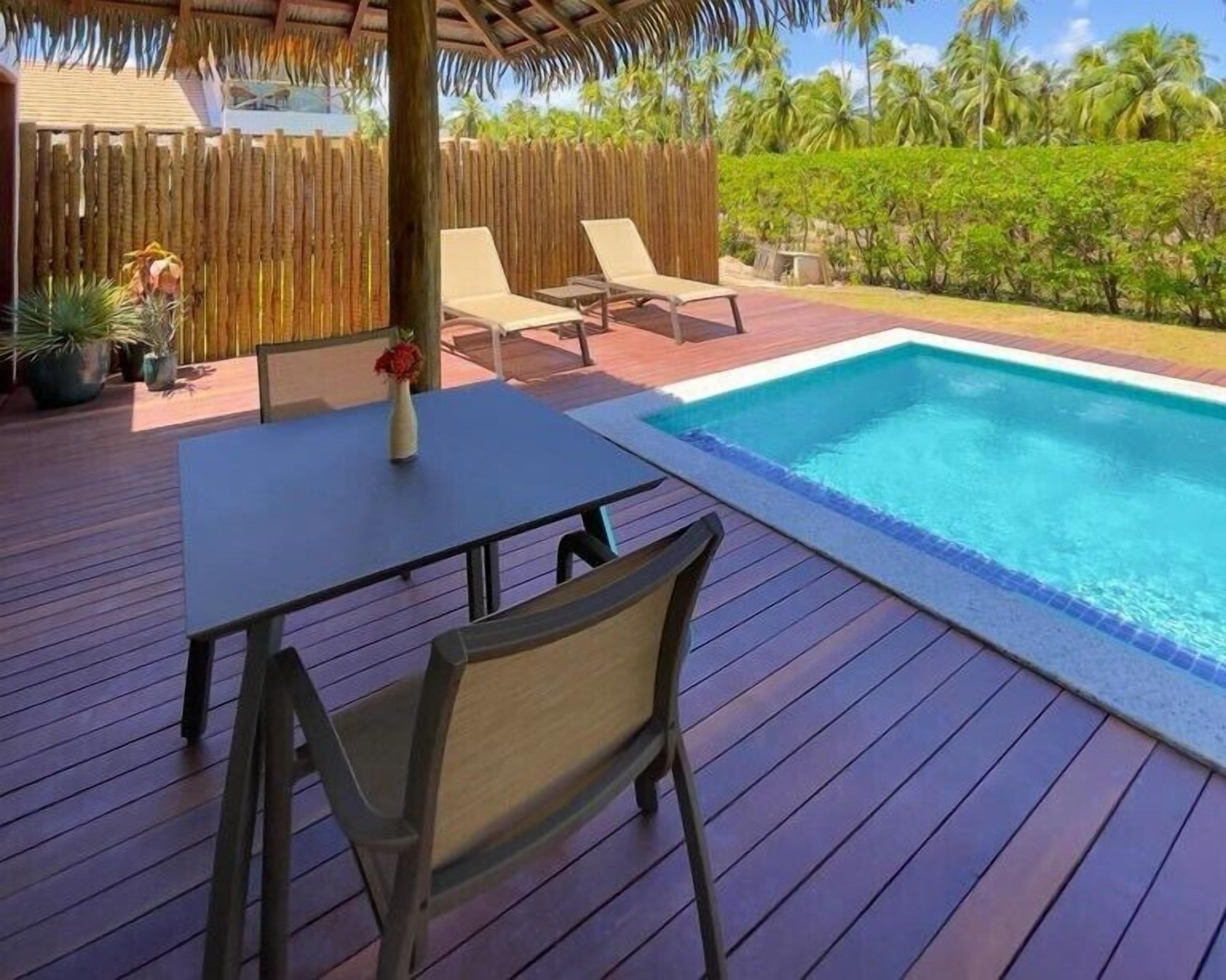 A wooden deck with a pool, lounge chairs, and a table with a vase of flowers.