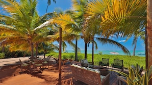 A wooden deck with wicker furniture, palm trees, and a view of the ocean. - Pousada Samba Pa Ti (Porto de Pedras)