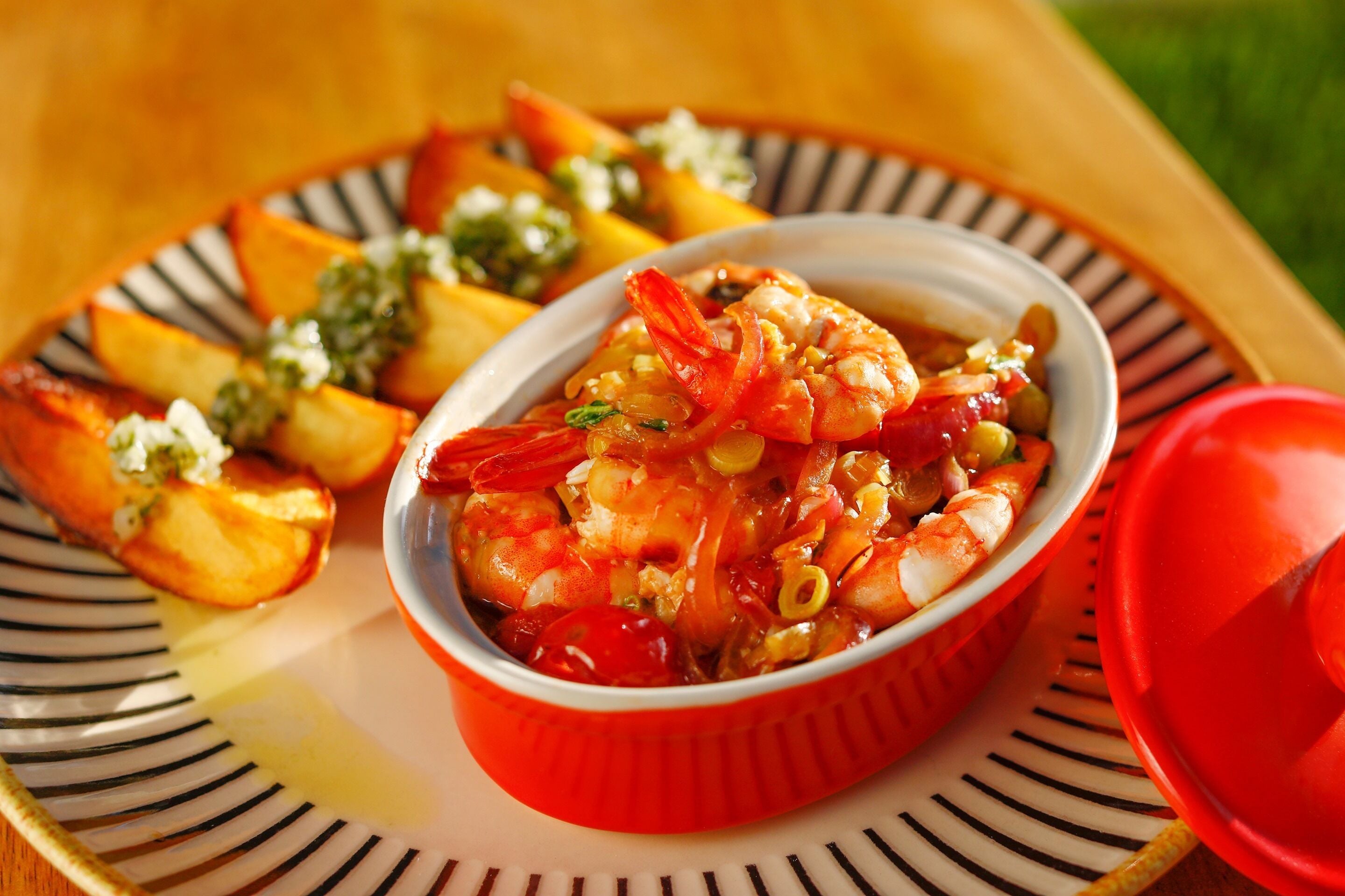 Un plato de camarones con verduras y un tazón rojo sobre un plato a rayas.