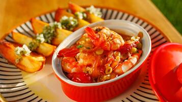 Un plato de camarones con verduras y un tazón rojo sobre un plato a rayas.
