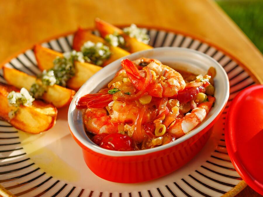 Un plato de camarones con verduras y un tazón rojo sobre un plato a rayas.