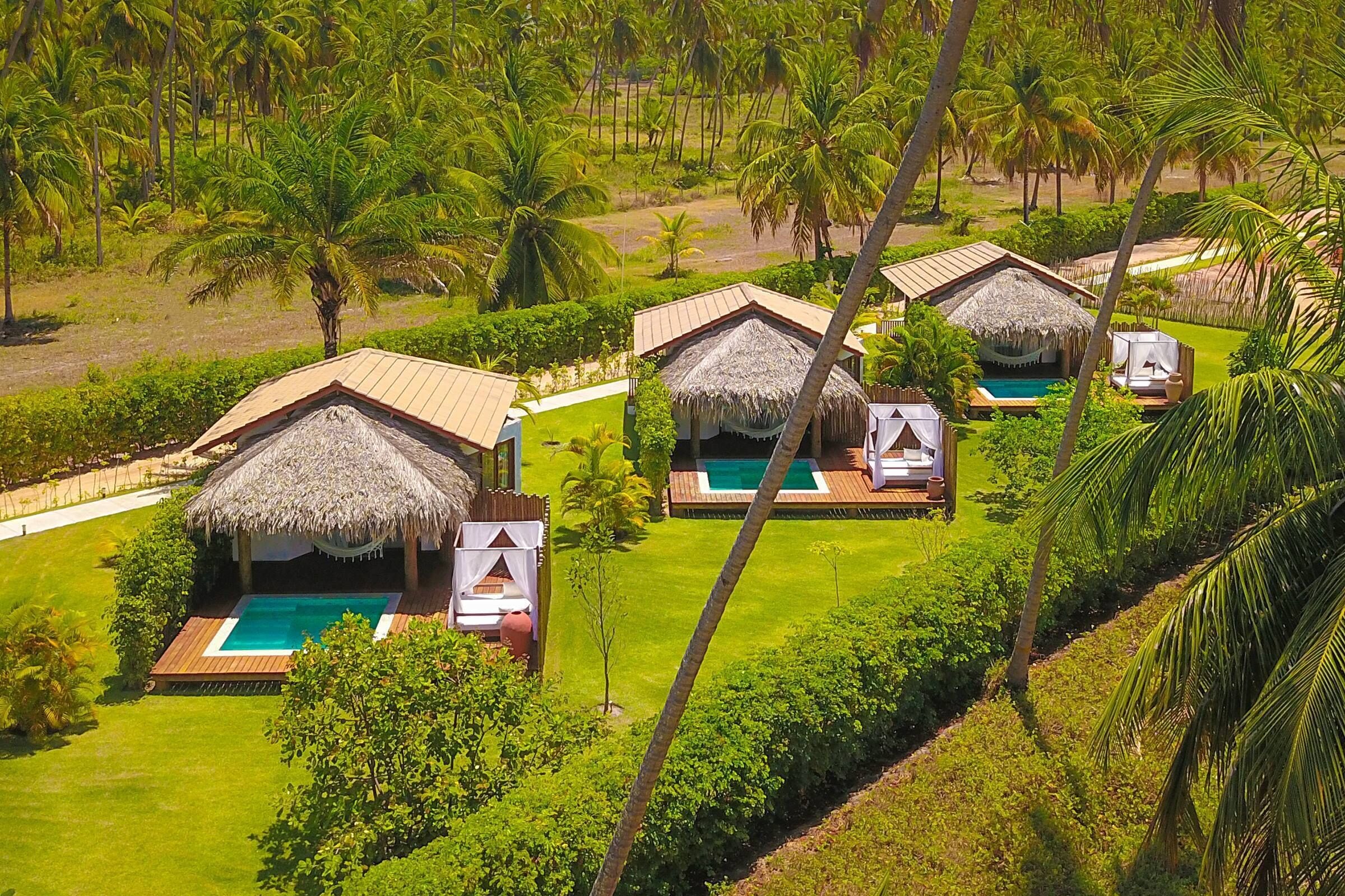 Un complexe hôtelier doté de bungalows aux toits de chaume, chacun ayant sa propre piscine et étant entouré d’une végétation luxuriante.