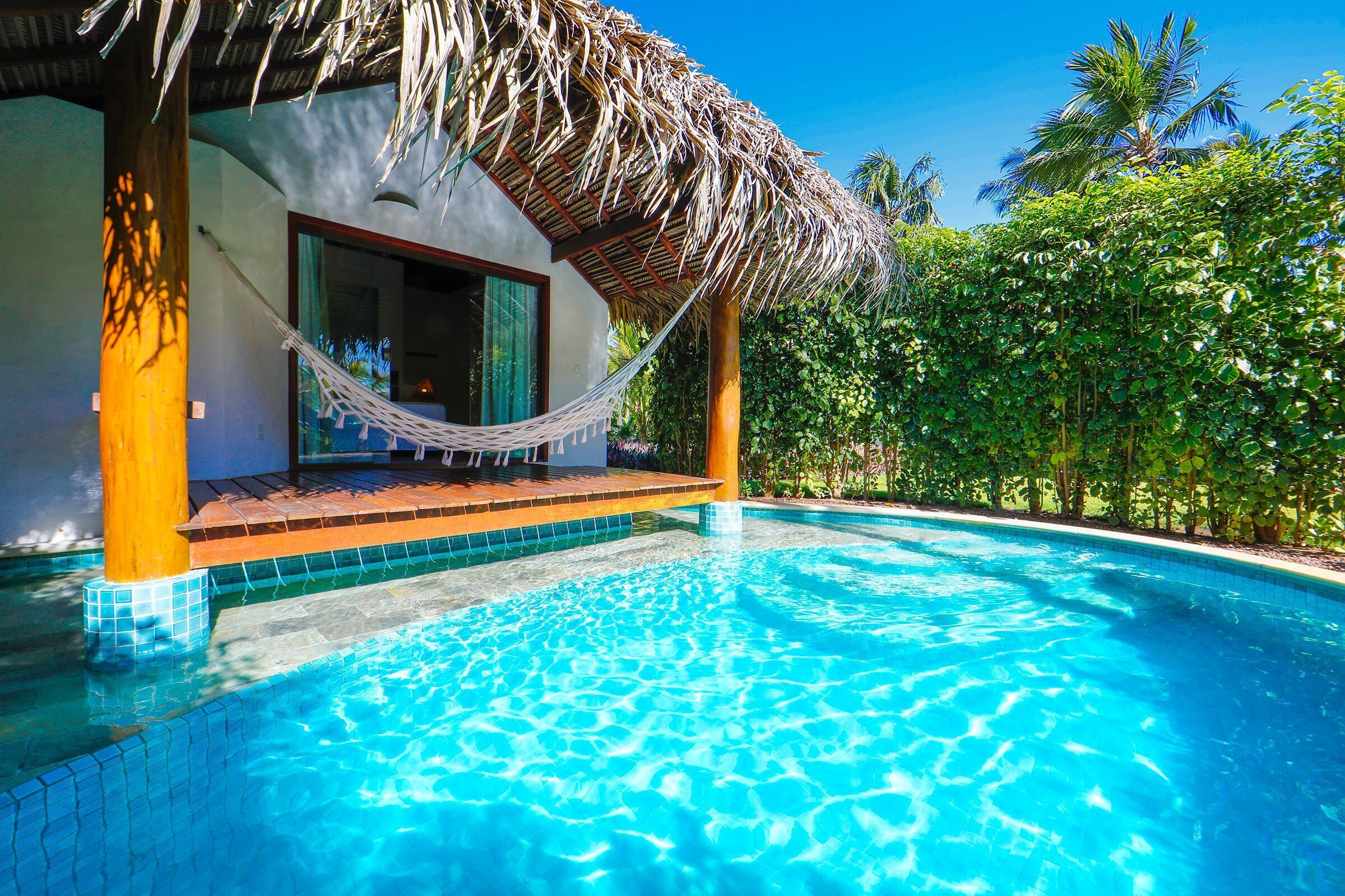 Una piscina azul cristalina con una estructura de techo de paja, rodeada de exuberante follaje.