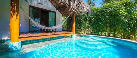 Una piscina azul cristalina con una estructura de techo de paja, rodeada de exuberante follaje.
