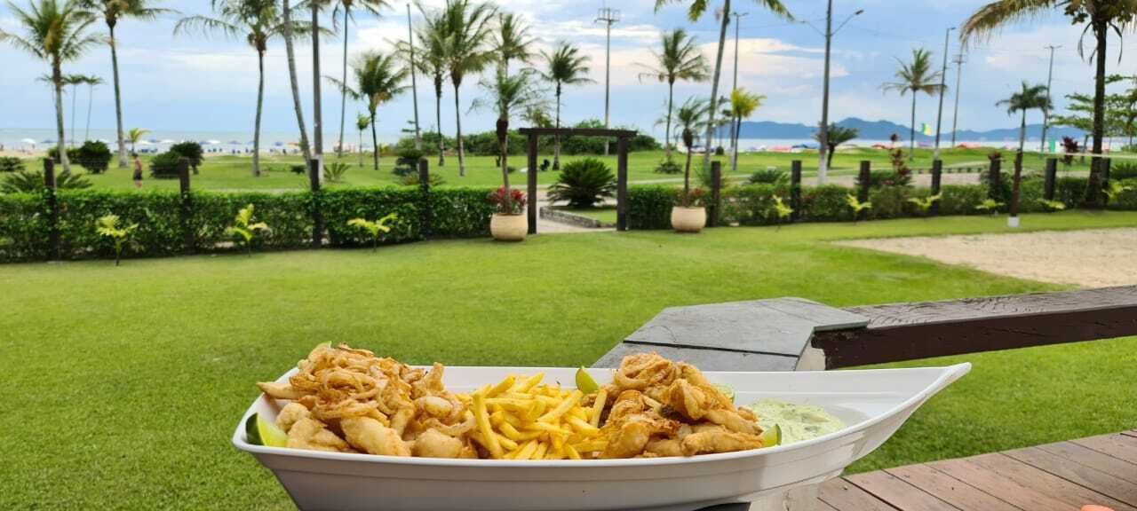 A bowl of fried chicken and fries on a table with a view of a well-maintained lawn and palm trees.