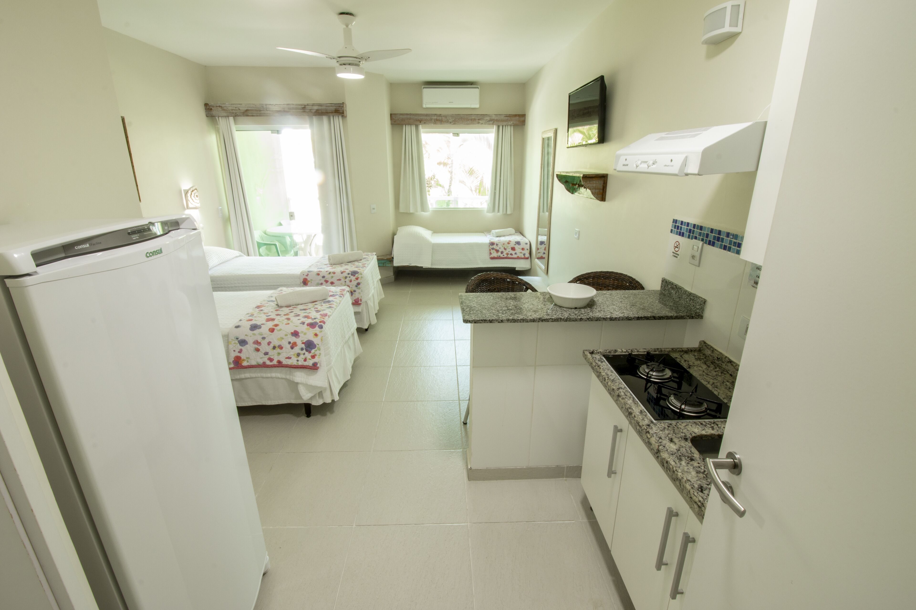 Habitación de hotel con kitchenette, una cama, una mesita y un ventanal con cortinas.