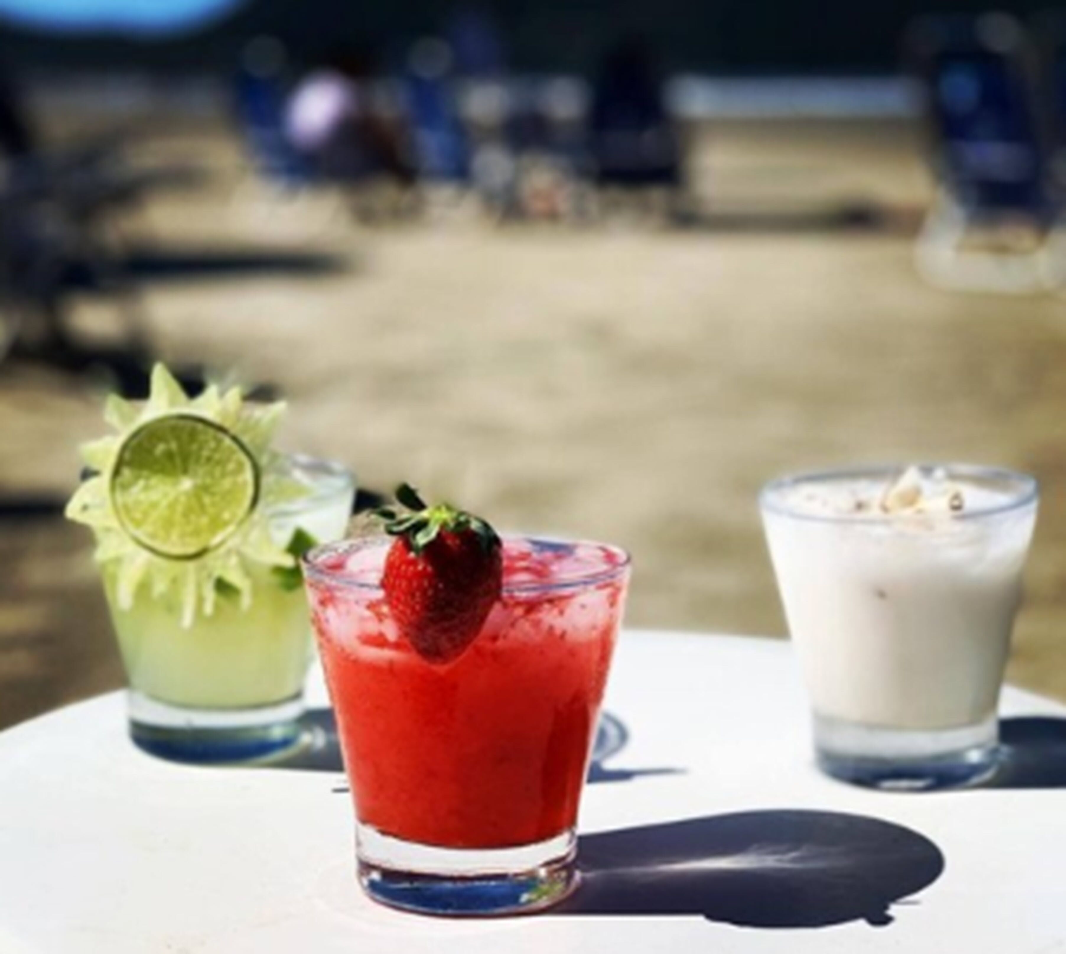 Three drinks on a table with a sandy background.