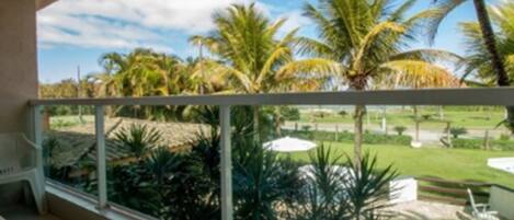 A balcony with a view of a tropical garden, including palm trees and a lawn.