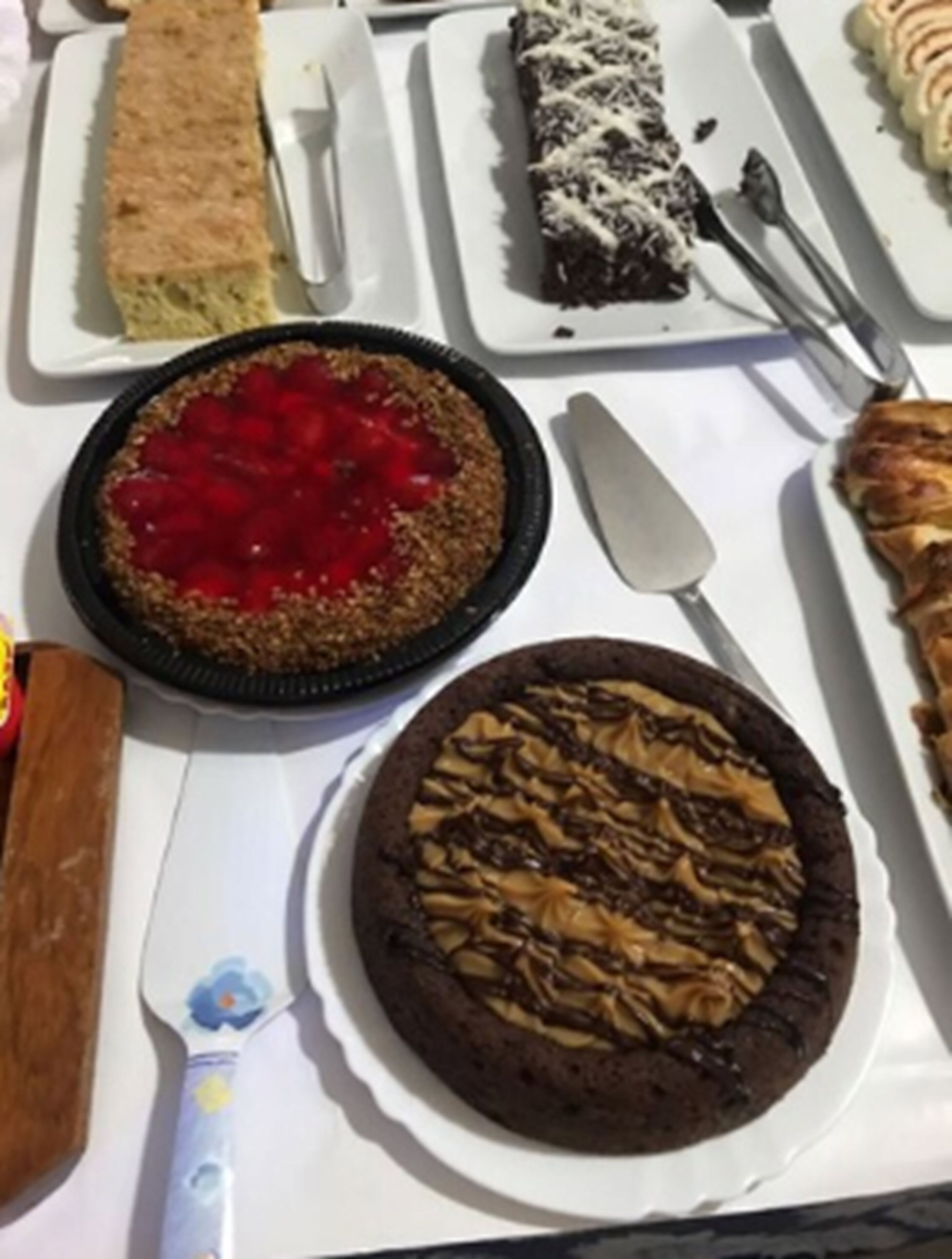 A variety of desserts on a table, including a pie with a red topping, a chocolate tart, and a cake with a nut topping.