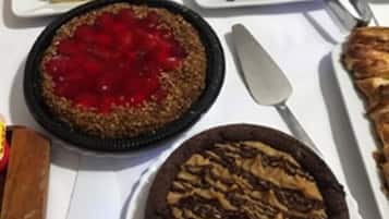 A variety of desserts on a table, including a pie with a red topping, a chocolate tart, and a cake with a nut topping.