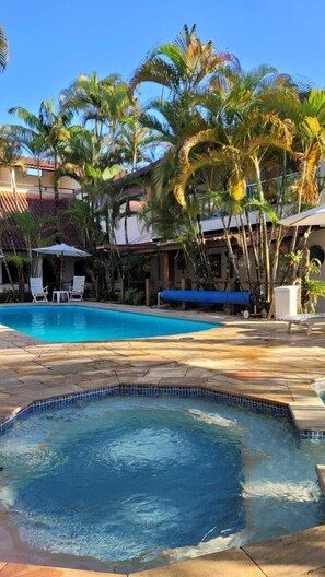 A swimming pool surrounded by palm trees and a covered seating area. - Apart Hotel Porto Kanoas (Bertioga)