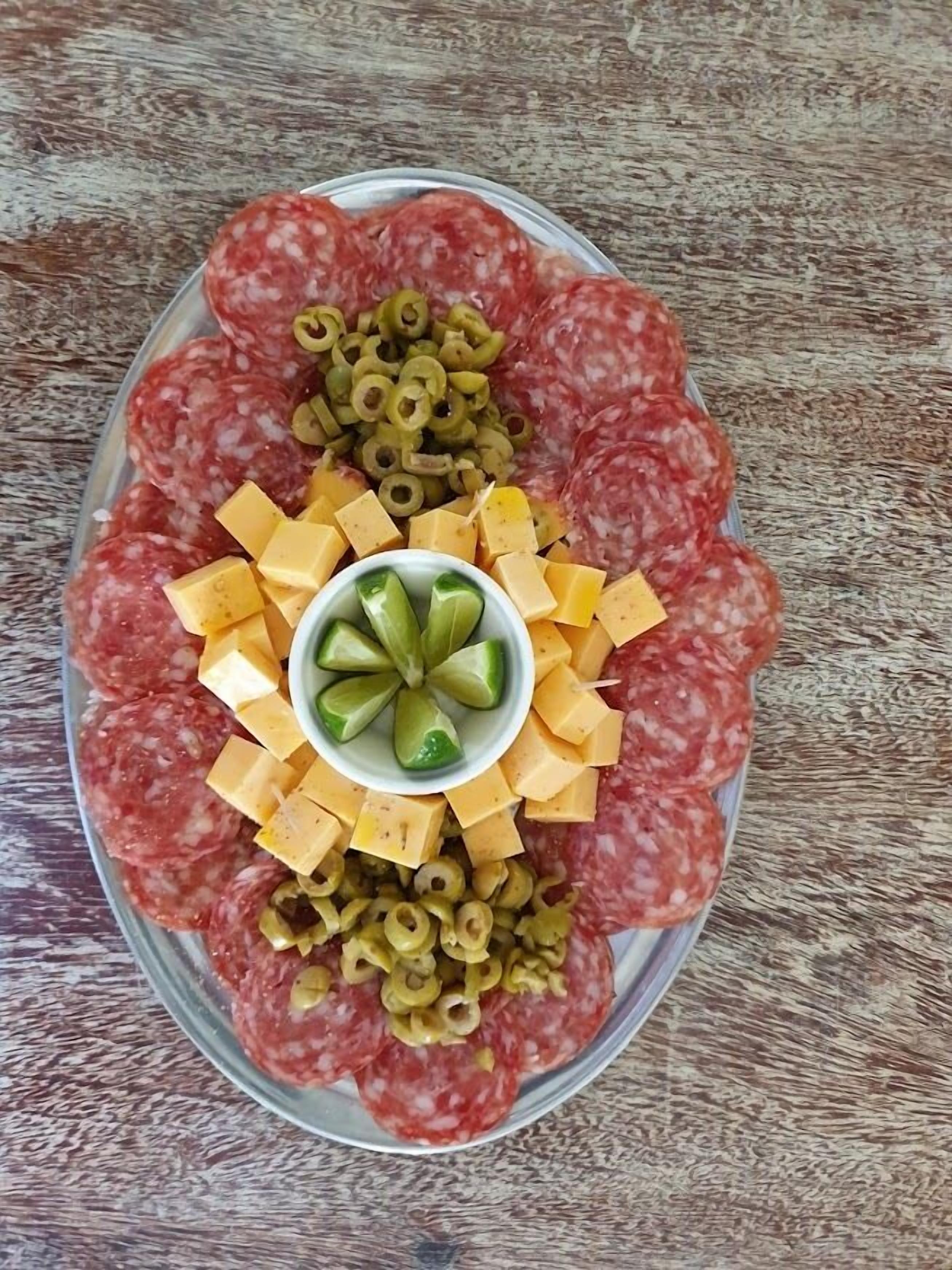 Une assiette de fines tranches de salami, de cubes de fromage et d’olives, disposés sur une table en bois.