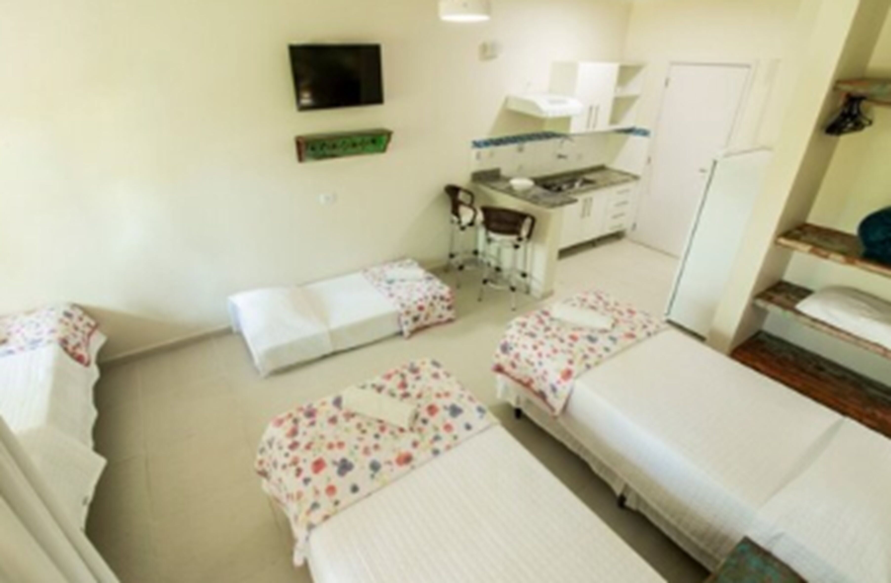 A hotel room with two single beds, a small kitchenette, a chair, and a television.