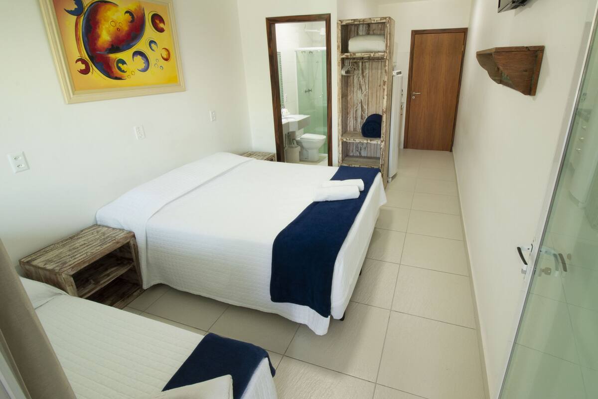 Habitación de hotel con cama, un banco de madera pequeño, zona de ducha y televisor montado en la pared.